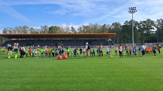 Zdjęcie przedstawiające boisko szkolne oraz dzieci biorące udział w zawodach sportowych.